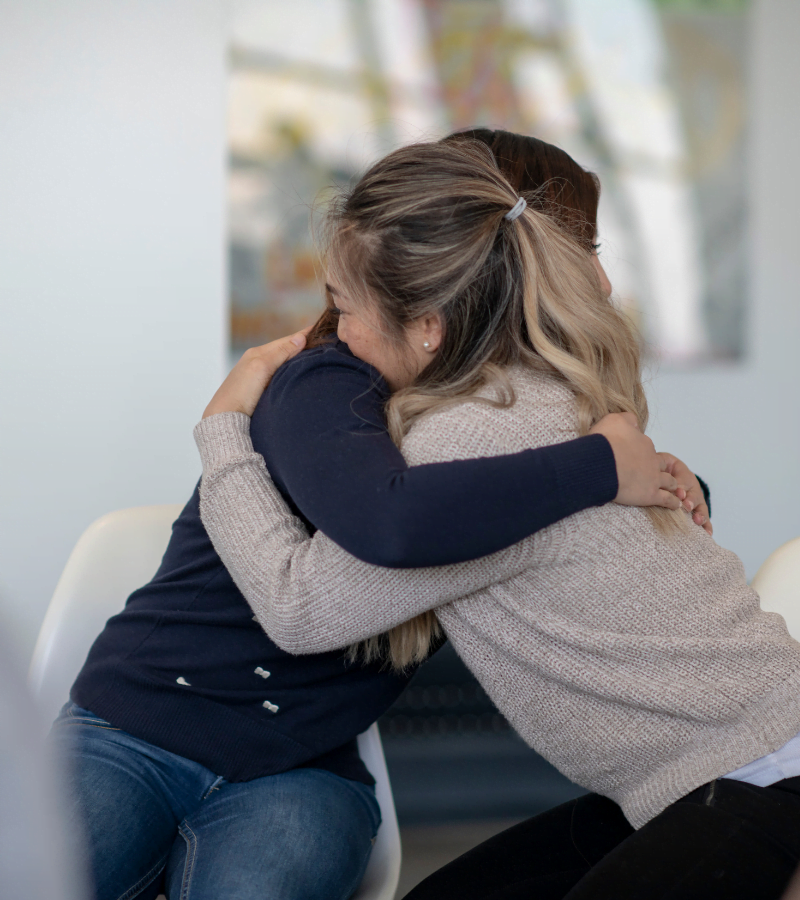 two women hugging during a group therapy session at a rehab facility